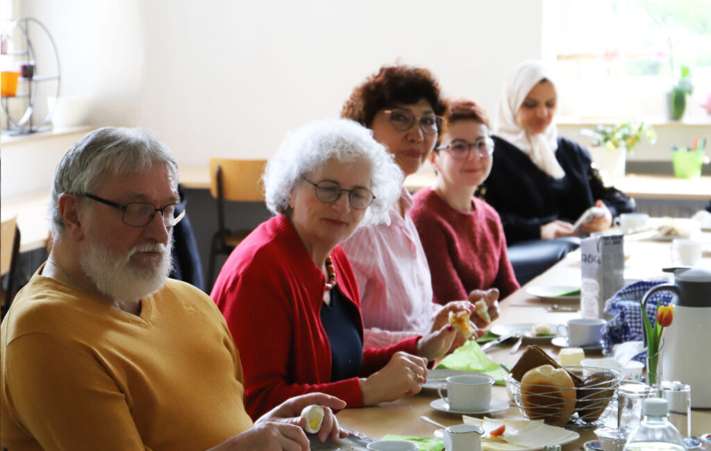 Fünf Menschen sitzen an einer gedeckten Frühstückstafel und schauen lächelnd in die Kamera