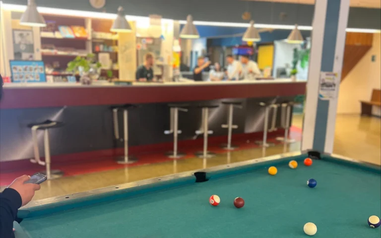 Aufnahme aus den Räumlichkeiten des Jugendtreffs Rheydt Side. Im Vordergrund ein Billiardtisch, auf dem gerade Billiard gespielt wird. Im Hintergrund unterhalten sich mehrere Menschen an einer langen Bar.