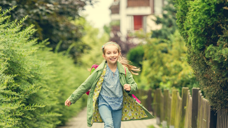 Ein fröhliches Schulkind geht über einen Fußweg durch frühlingshaft grüne Gärten