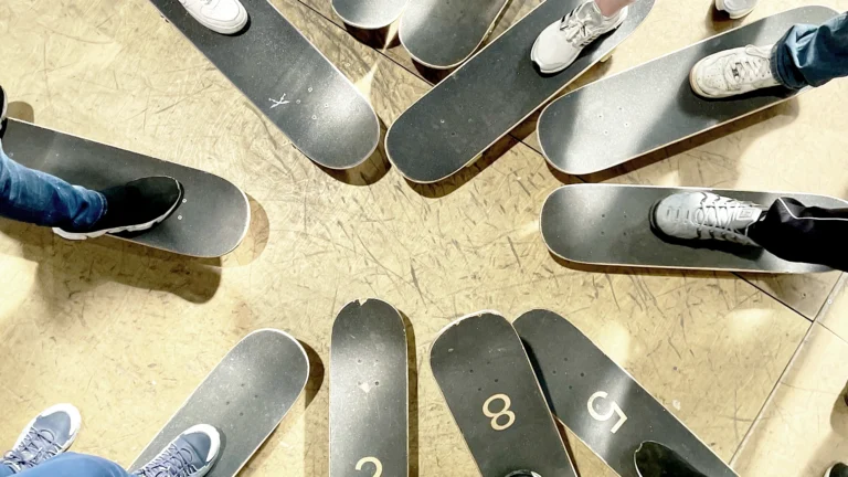 Ein Kreis aus Skateboards, auf denen die Füße und beine von jugendlichen Skatern zu sehen sind. Die Jugendlichen selbst sind außerhalb des Bildes, aber die zueinander zeigenden Skateboards symbolisieren Gemeinschaft und Zusammenhalt.