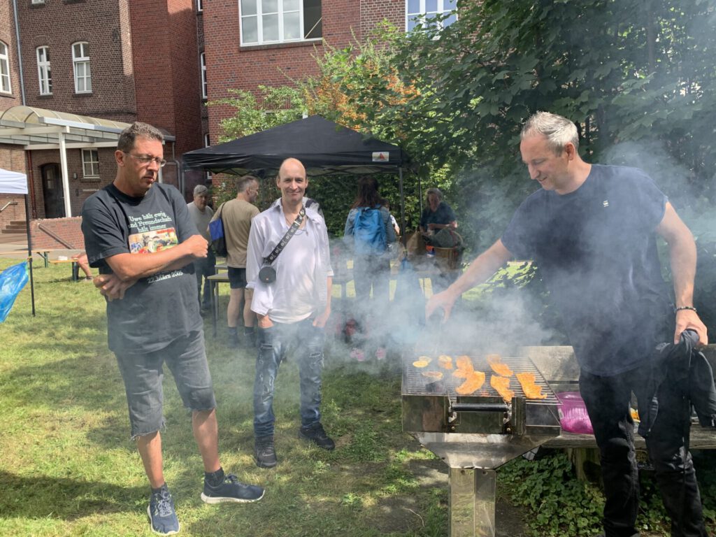Menschen stehen um einen rauchenden Grill